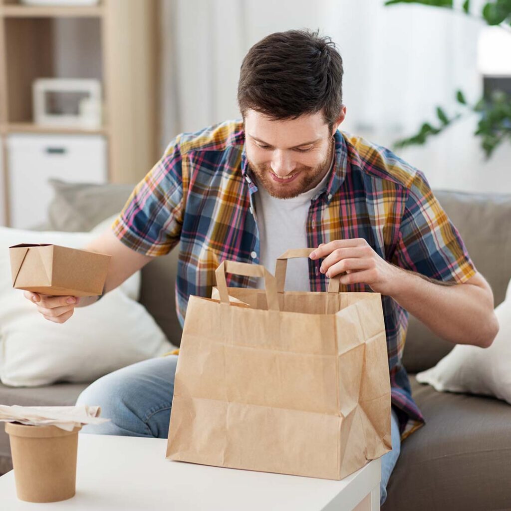 Photo of a man opening a grocery bag of food, with a happy look on his face